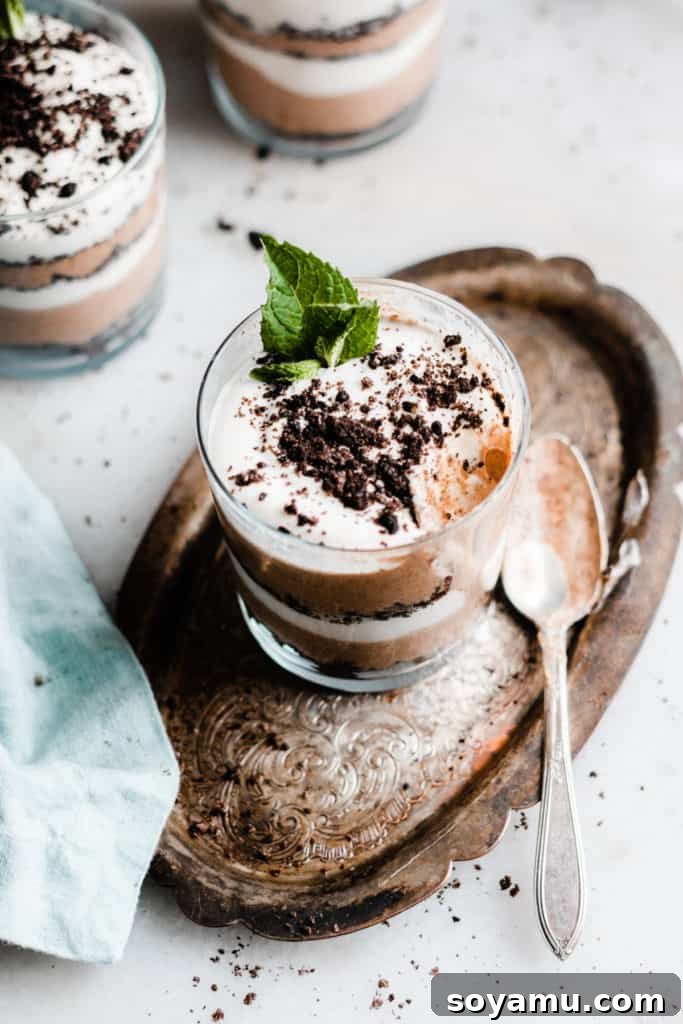 Bailey's Chocolate Mousse Parfaits - Silky smooth layers of Irish cream-infused whipped cream, chocolate whipped cream, and crushed oreos make up these delightful personal-sized desserts! These desserts are so easy to make and are no-bake! Perfect for St. Patrick's Day or any other celebration. Finished Bailey's Chocolate Mousse Parfait garnished with crushed Oreos and a mint sprig