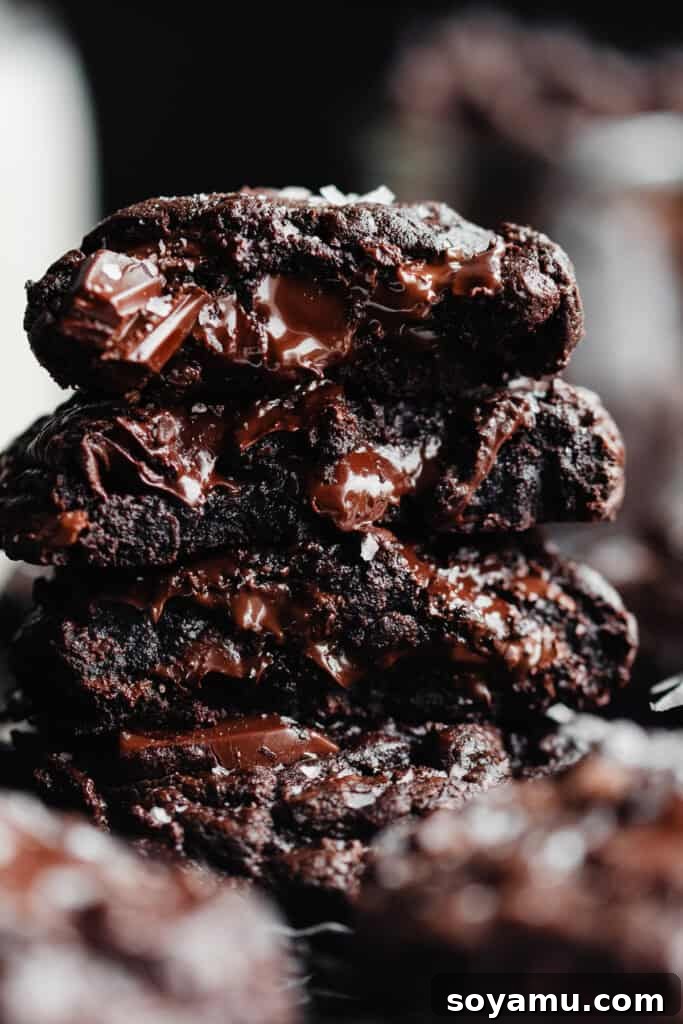 Triple Chocolate Chunk Cookies - World, meet Triple Chocolate Chunk Cookies! Ultra fudgy, with crackly tops - and three kinds of chocolate chunks! We're mixing semi-sweet, milk, and dark chocolate to make the richest possible chocolate cookie. Sprinkle some flaky sea salt over those melted pools of chocolate and dive in to dessert heaven! #chocolatecookies #cookierecipes #dessertrecipes #cookies #chocolaterecipes #chocolatedesserts #bluebowlrecipes | bluebowlrecipes.com A close-up on a stack of triple chocolate cookie halves, revealing their incredibly fudgy and gooey interiors, showcasing the variety of melted chocolate chunks.