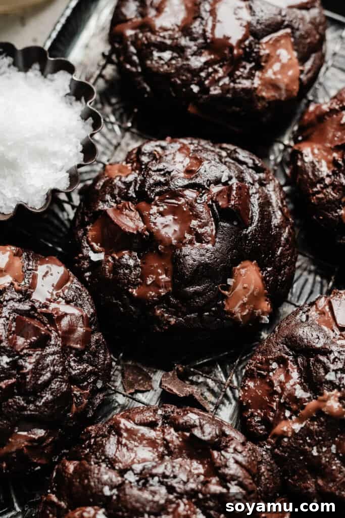 Triple Chocolate Chunk Cookies - World, meet Triple Chocolate Chunk Cookies! Ultra fudgy, with crackly tops - and three kinds of chocolate chunks! We're mixing semi-sweet, milk, and dark chocolate to make the richest possible chocolate cookie. Sprinkle some flaky sea salt over those melted pools of chocolate and dive in to dessert heaven! #chocolatecookies #cookierecipes #chocolaterecipes #chocolatedesserts #bluebowlrecipes | bluebowlrecipes.com A close-up on triple chocolate cookies cooling on a vintage wire rack, showing their rich color and inviting texture.