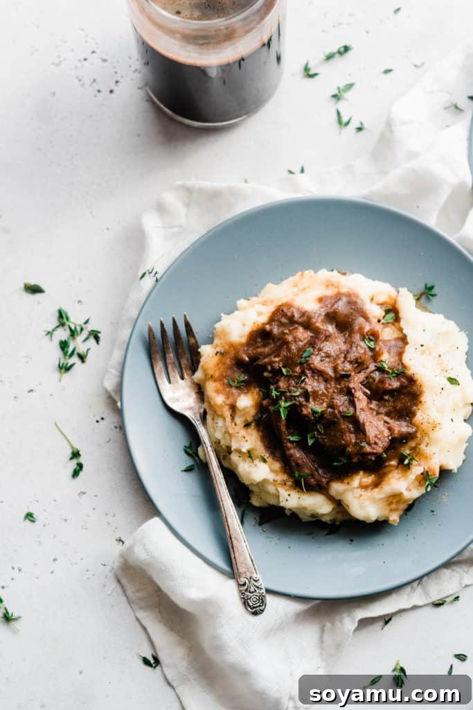 Cheddar Mashed Potatoes with Fall-Apart Short Ribs. A close-up of cheddar mashed potatoes topped with incredibly tender, shredded beer braised short ribs, drizzled with rich sauce.