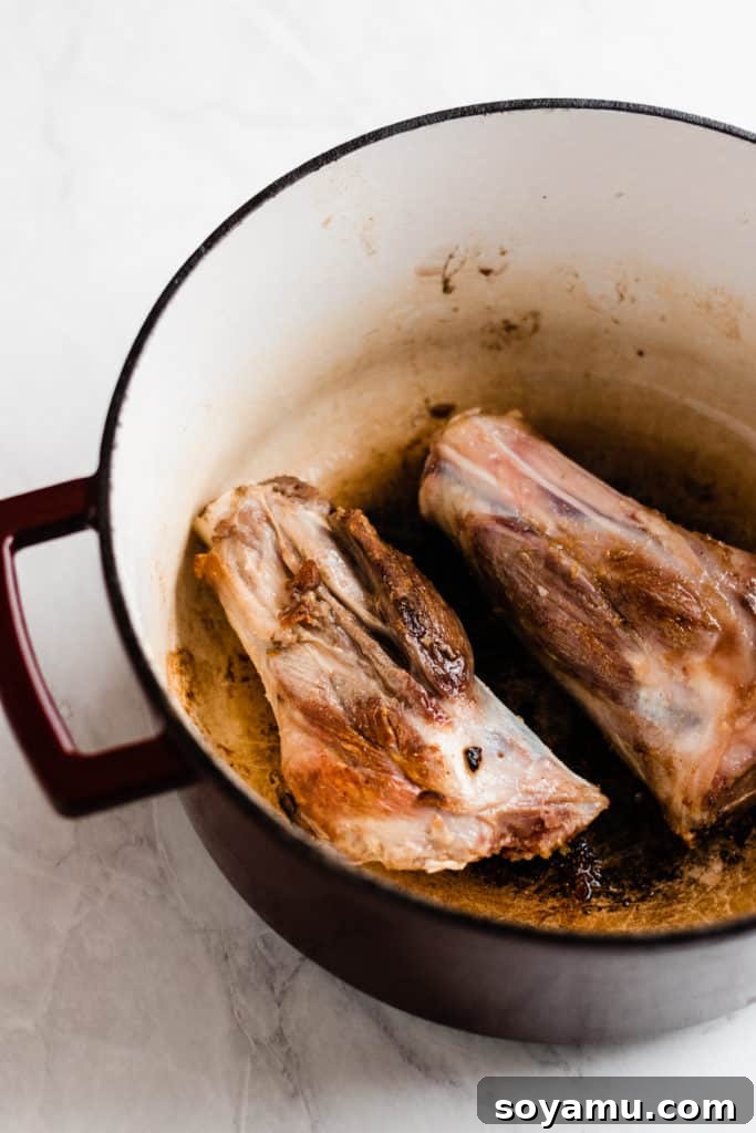 Searing lamb shanks for rich flavor development Uncooked lamb shanks seasoned in a Dutch oven with olive oil