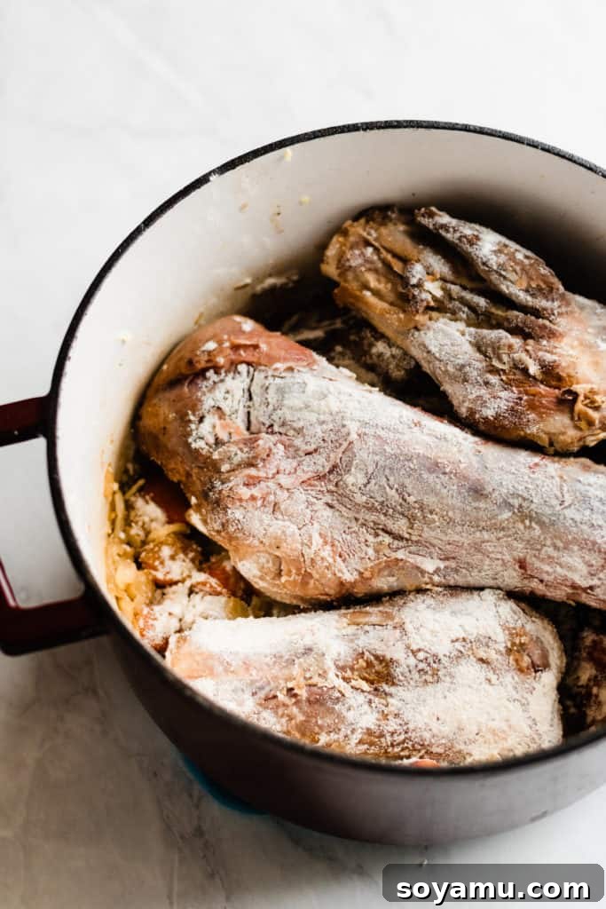 Building the flavor base with vegetables and floured lamb Lamb shanks coated in flour, resting on a bed of sautéed carrots and onions in a Dutch oven