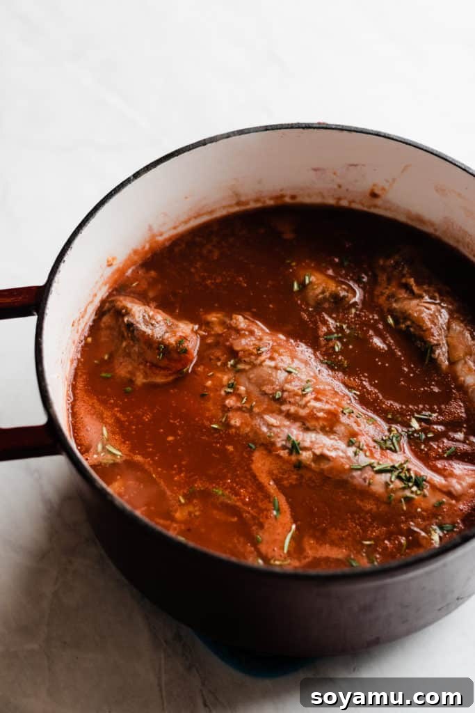 Lamb shanks braising in aromatic red wine sauce Lamb shanks simmering in a rich red wine sauce with vegetables and herbs in a Dutch oven