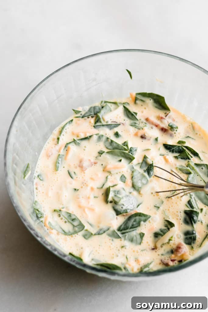 Mini Quiche Cups with Spinach, Bacon, and Cheddar - Made with store-bought puff pastry, filled with a delicious smoky, flavorful mixture of gruyere and cheddar cheese, spinach, bacon, eggs, and milk. Perfect for Easter brunch. #easterrecipes #brunchrecipes #quiche #breakfastrecipes #brunch #easterbrunch #spinachquiche #bacon #miniquiche A closer view of the well-mixed quiche filling, ready for assembly.