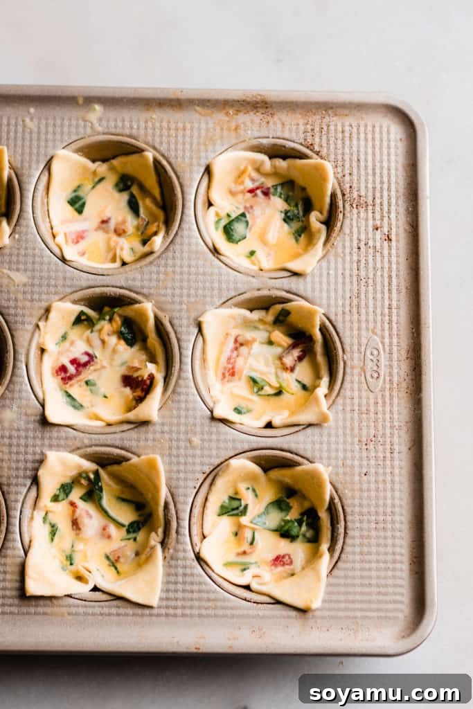 Mini Quiche Cups with Spinach, Bacon, and Cheddar - Made with store-bought puff pastry, filled with a delicious smoky, flavorful mixture of gruyere and cheddar cheese, spinach, bacon, eggs, and milk. Perfect for Easter brunch. #easterrecipes #brunchrecipes #quiche #breakfastrecipes #brunch #easterbrunch #spinachquiche #bacon #miniquiche Mini quiche cups with filling nestled in puff pastry squares in a muffin tin, ready to be baked.