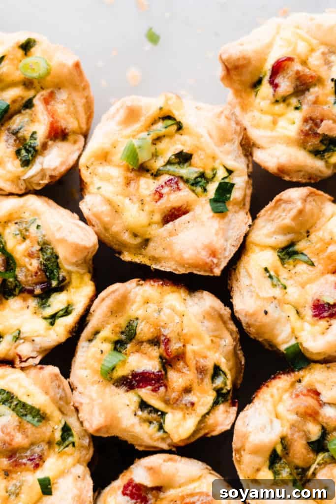 Mini Quiche Cups with Spinach, Bacon, and Cheddar - Made with store-bought puff pastry, filled with a delicious smoky, flavorful mixture of gruyere and cheddar cheese, spinach, bacon, eggs, and milk. Perfect for Easter brunch. #easterrecipes #brunchrecipes #quiche #breakfastrecipes #brunch #easterbrunch #spinachquiche #bacon #miniquiche A close-up view of multiple baked mini quiche cups nestled closely together, showcasing their texture.