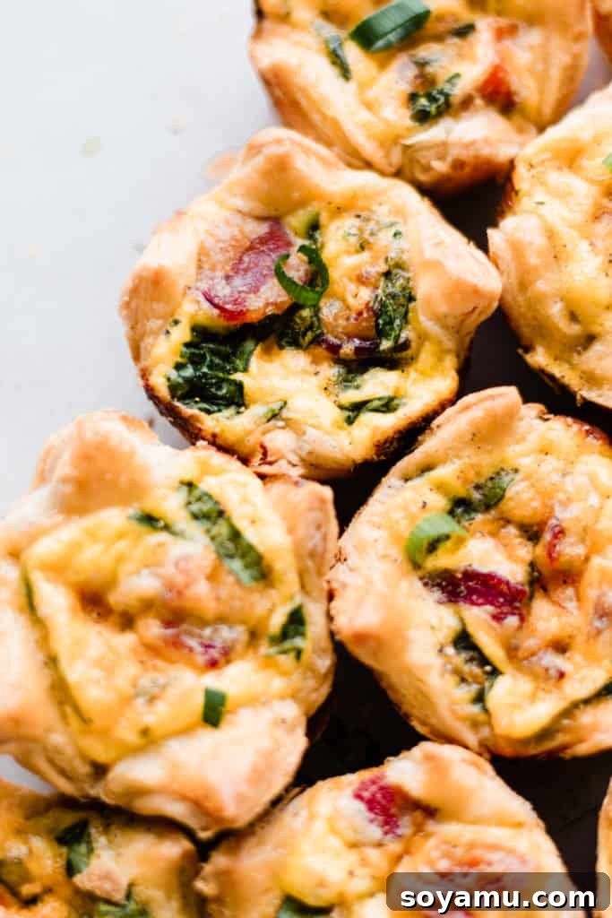 Mini Quiche Cups with Spinach, Bacon, and Cheddar - Made with store-bought puff pastry, filled with a delicious smoky, flavorful mixture of gruyere and cheddar cheese, spinach, bacon, eggs, and milk. Perfect for Easter brunch. #easterrecipes #brunchrecipes #quiche #breakfastrecipes #brunch #easterbrunch #spinachquiche #bacon #miniquiche A close-up of mini quiche cups, showcasing their golden-brown tops and rich, inviting filling.