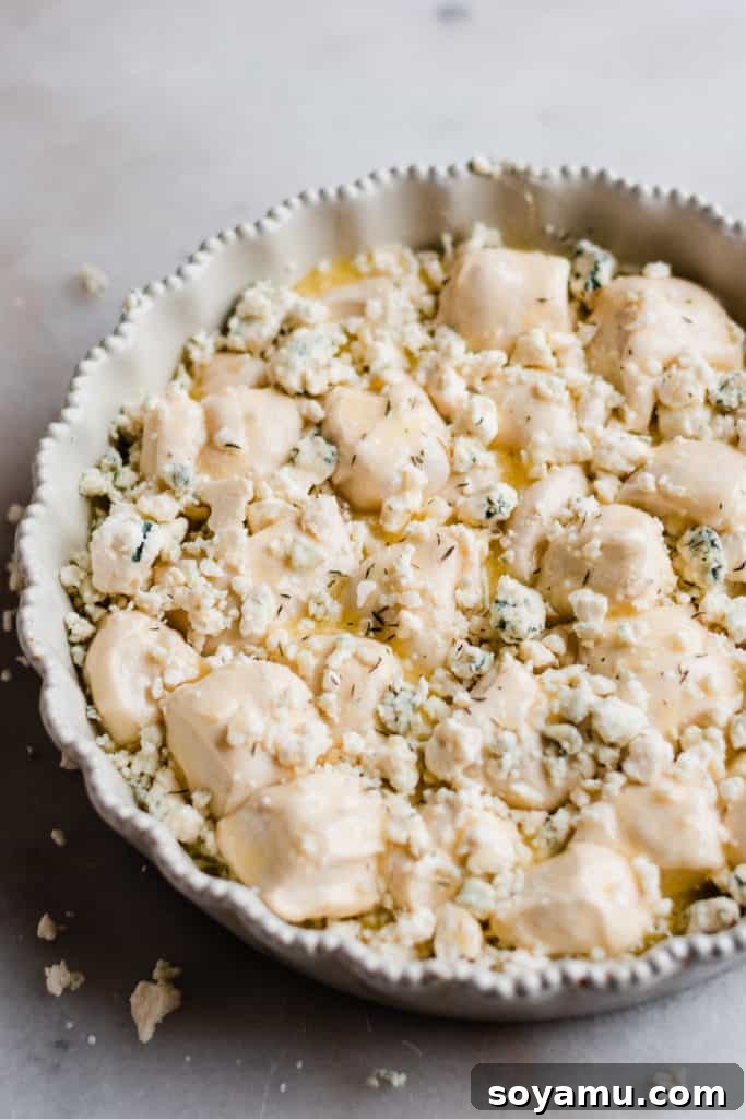Bread dough pieces in a pan, generously topped with crumbled cheese and garlic powder, ready for baking.