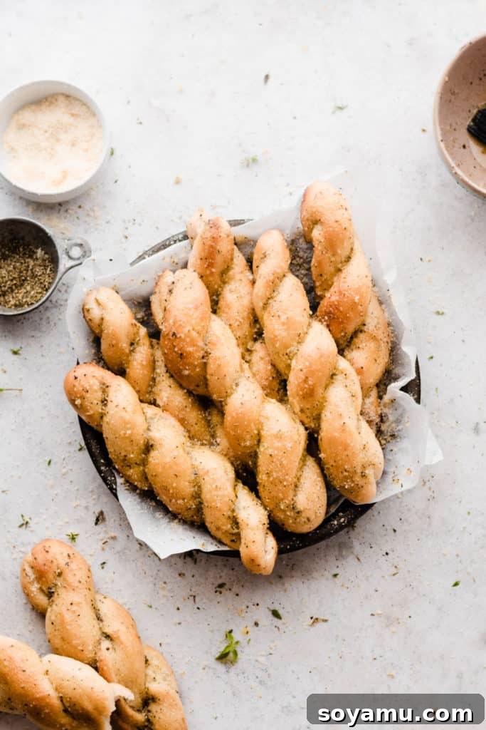 A plate full of buttery twisted breadsticks sprinkled with parmesan and herbs, ready to be enjoyed.