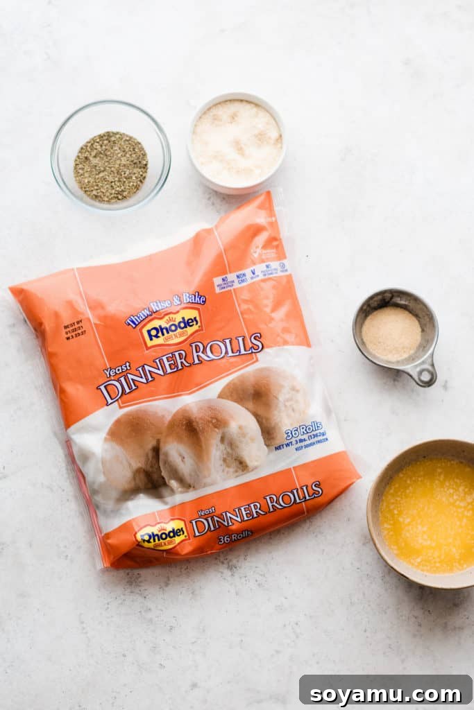 A package of Rhodes Dinner Roll dough on a smooth surface, surrounded by bowls of melted butter, Italian seasoning, garlic powder, and grated parmesan cheese – all the simple ingredients needed.