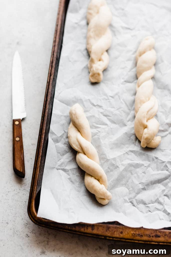 A close-up view of three twisted, unbaked breadsticks neatly arranged on a sheet pan, perfectly formed and ready for the oven.