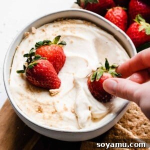 A hand dipping a strawberry into the bowl of cheesecake dip.