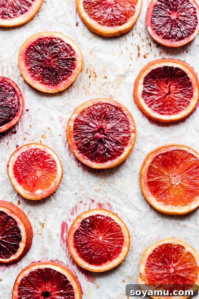 Thinly sliced blood oranges arranged on a parchment-lined baking sheet, ready for roasting
