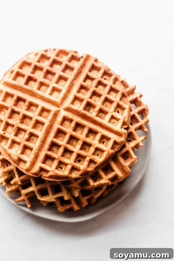 A stack of golden-brown, crispy buttermilk waffles piled high on a white plate