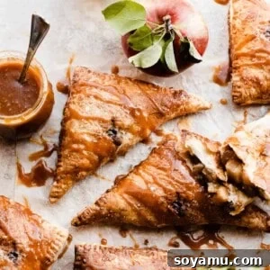 Puff pastry apple turnovers on a light surface with salted caramel sauce drizzled on and whole apples around.