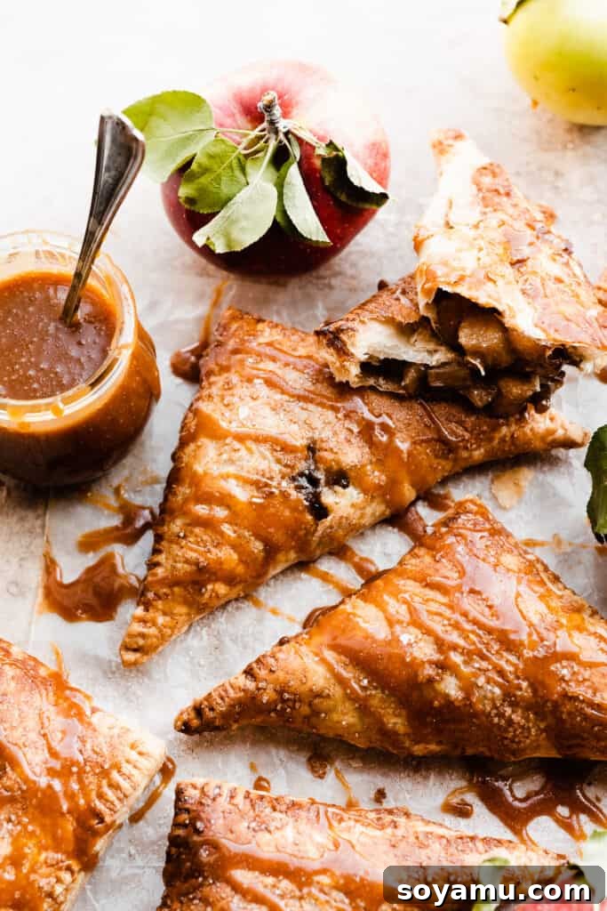 Flaky Caramel Apple Pockets 9 Apple turnovers drizzled with salted caramel sauce, with one broken open near a jar of caramel sauce.
