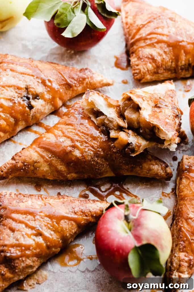 Flaky Caramel Apple Pockets 10 Apple turnovers drizzled with salted caramel sauce, with one broken open near some whole apples.