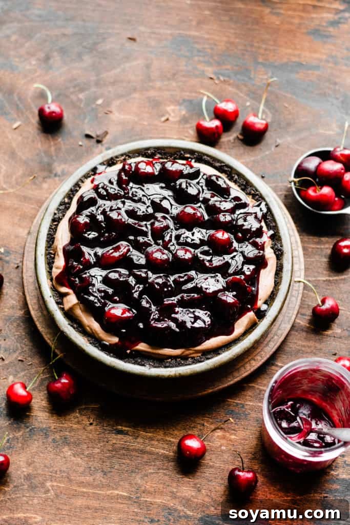 The dark chocolate mousse filling in a rich chocolate pie crust, generously topped with a glistening layer of vibrant cherry sauce, ready for the final whipped cream layer.