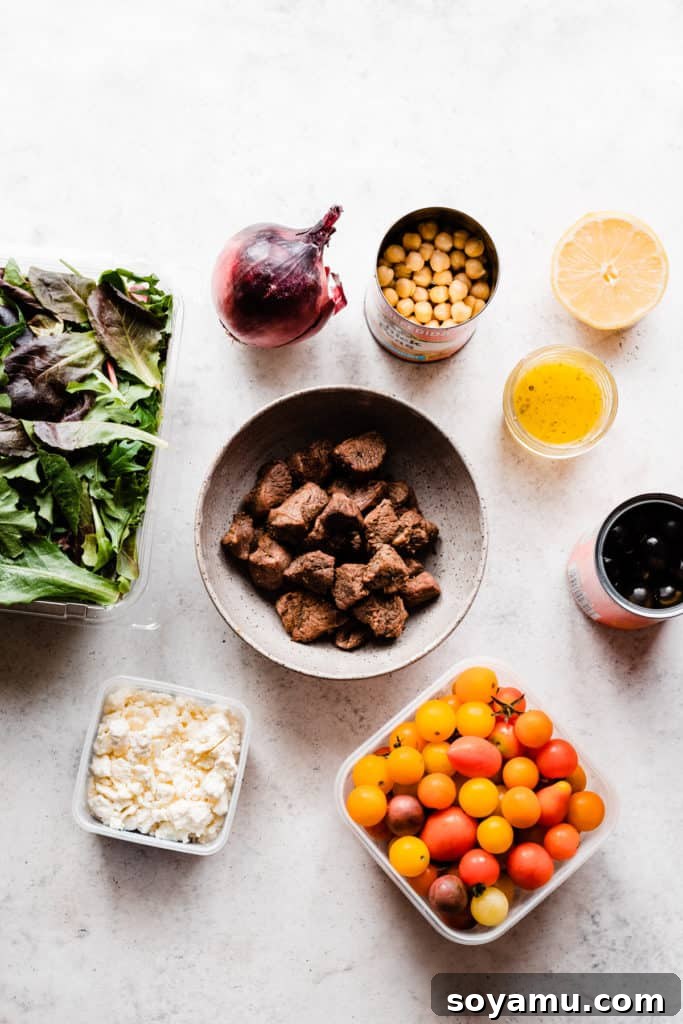 Zesty Lemon Grilled Lamb Power Bowls 4 A smooth kitchen surface showcasing all the fresh salad ingredients laid out: crisp lettuce, a vibrant red onion, canned chickpeas, creamy feta cheese, sweet cherry tomatoes, and briny black olives, ready for assembly
