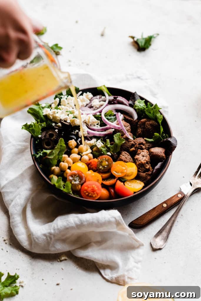 Zesty Lemon Grilled Lamb Power Bowls 5 A hand is shown pouring the vibrant yellow lemon dressing from a glass jar over a beautifully assembled salad bowl, highlighting the final touch before serving