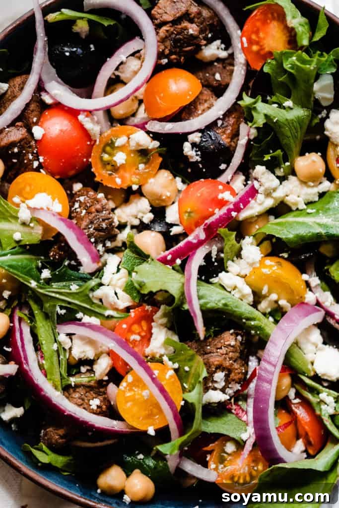 Zesty Lemon Grilled Lamb Power Bowls 7 A close-up view of the tossed salad, highlighting the vibrant mix of thinly sliced red onion, fresh lettuce, halved cherry tomatoes, crumbled feta, briny black olives, and tender grilled lamb pieces, all coated in dressing