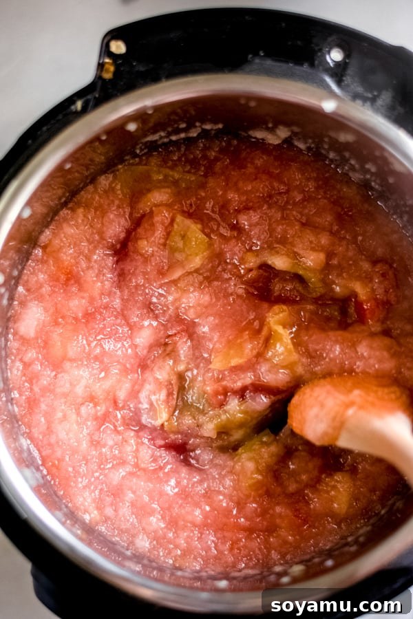 Pureed applesauce in an Instant Pot being stirred with a wooden spoon, showing its creamy texture.