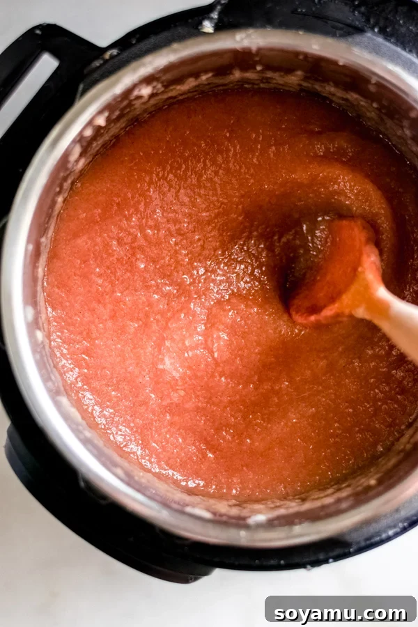 Thickening the applesauce in the Instant Pot with a wooden spoon after adding sugar and spices.