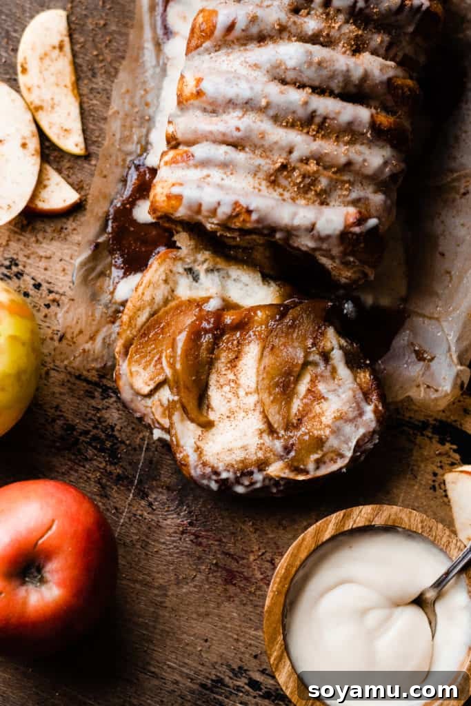 Gooey Caramel Apple Monkey Bread 2 A golden-brown loaf of Caramel Apple Pull Apart Bread on a rustic wooden surface, surrounded by fresh apples and a bowl of creamy maple glaze, evoking the cozy essence of fall baking.