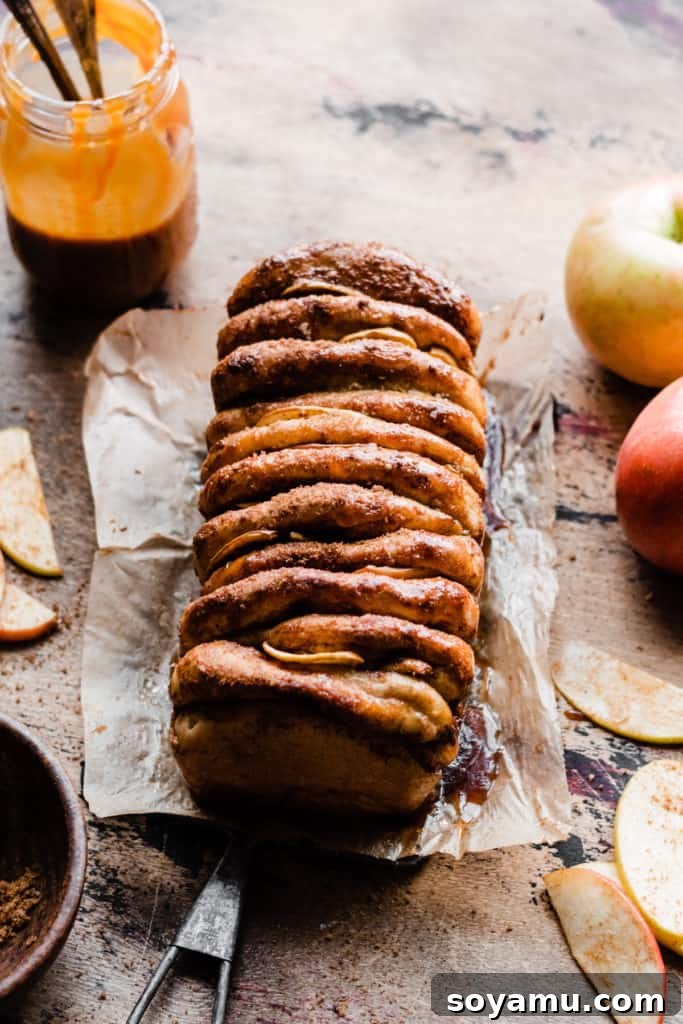 Gooey Caramel Apple Monkey Bread 5 The stunning, golden-brown baked loaf of Caramel Apple Pull Apart Bread, removed from its pan and resting on a wooden surface, with a jar of rich caramel sauce and fresh apples nearby, ready for glazing and serving.