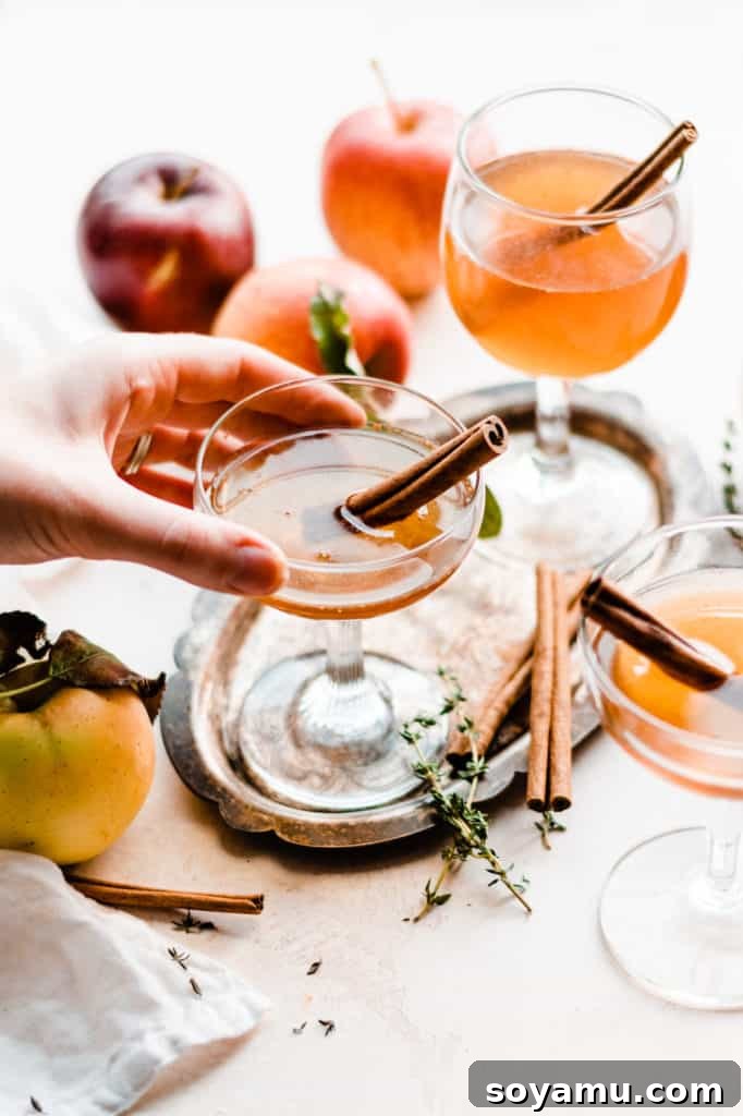 Maple Crisp Old Fashioned 3 A hand gracefully reaching for a beautifully presented glass of the apple cider old fashioned cocktail, showcasing its rich amber hue and inviting ambiance.