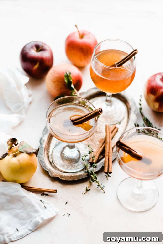 Maple Crisp Old Fashioned 5 Three stemmed glasses brimming with Apple Cider Old Fashioneds, elegantly arranged with fresh apple slices and cinnamon sticks, creating a visually appealing autumn tableau.