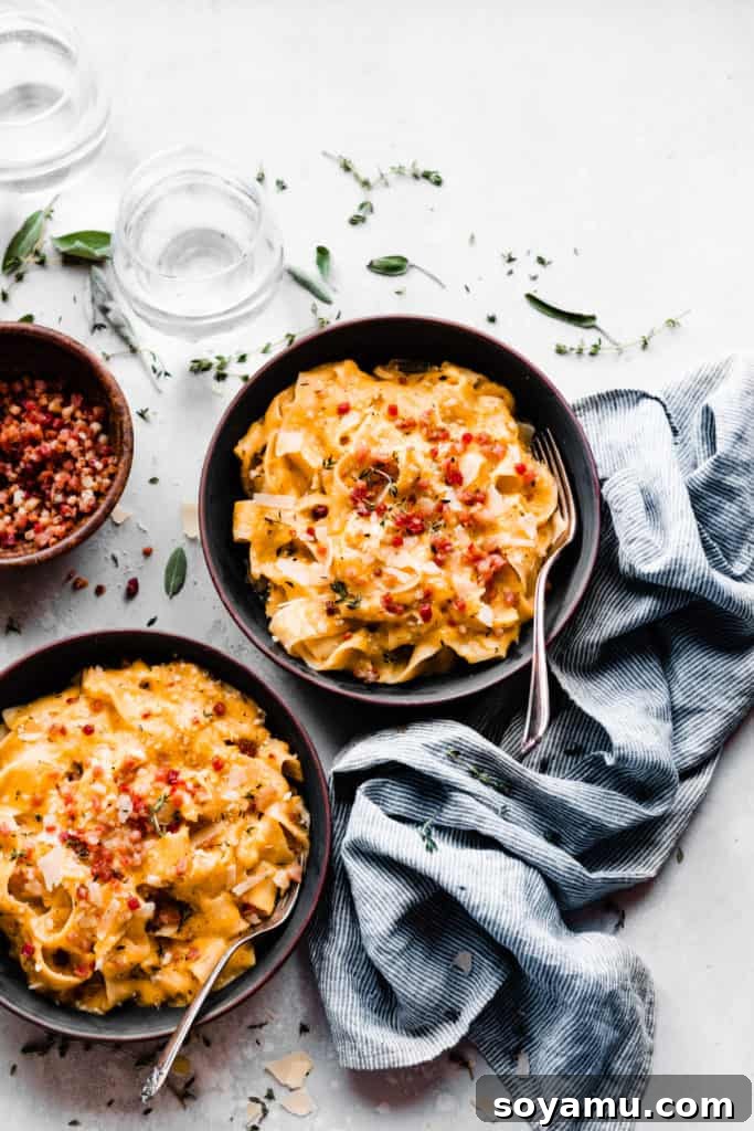 Velvet Butternut Pasta with Savory Pancetta 2 Two generously filled bowls of creamy butternut squash pasta topped with crispy pancetta, resting on a rustic gray surface. Fresh herbs and water glasses complete the inviting scene, emphasizing comfort and warmth.