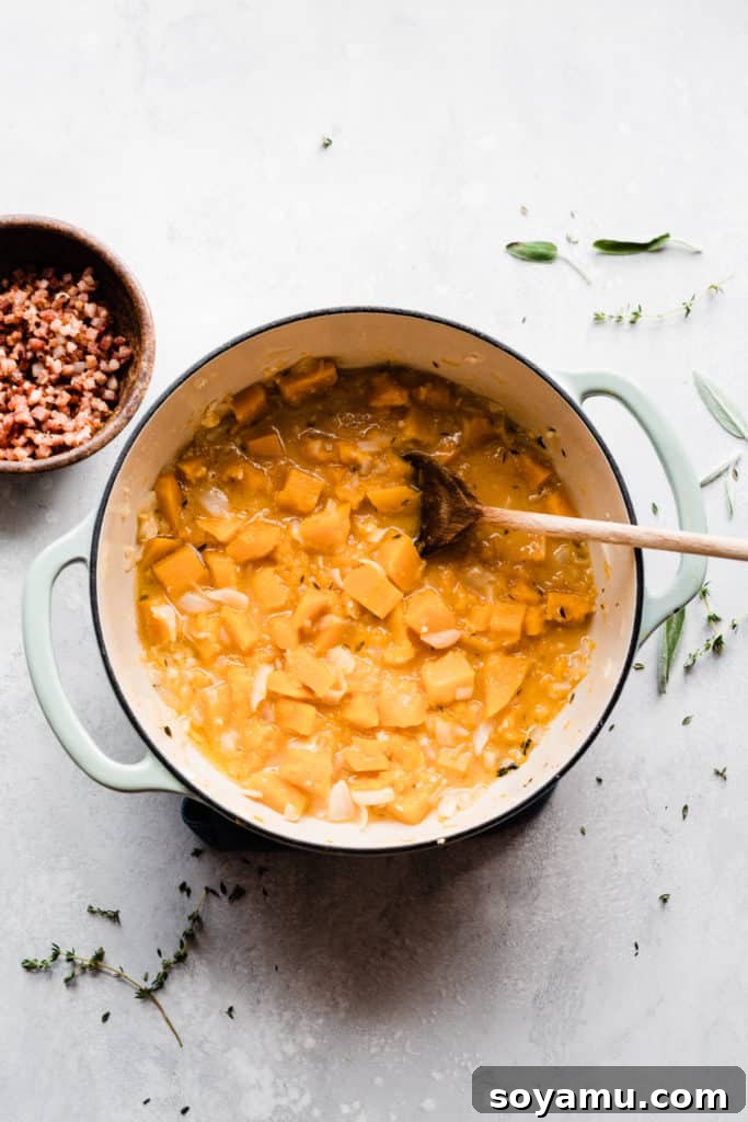 Velvet Butternut Pasta with Savory Pancetta 5 A Dutch oven is filled with vibrant orange cubes of butternut squash simmering in a savory broth, perfectly positioned next to a bowl of golden, crispy pancetta, ready to be incorporated.