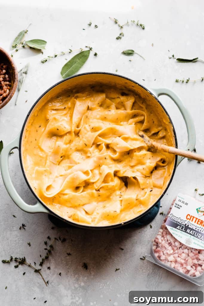 Velvet Butternut Pasta with Savory Pancetta 7 A Dutch oven showcases ribbons of perfectly cooked pasta generously coated in a rich, creamy butternut squash sauce, surrounded by a bowl of golden, crispy pancetta and scattered fresh herbs, hinting at the delicious final plating.