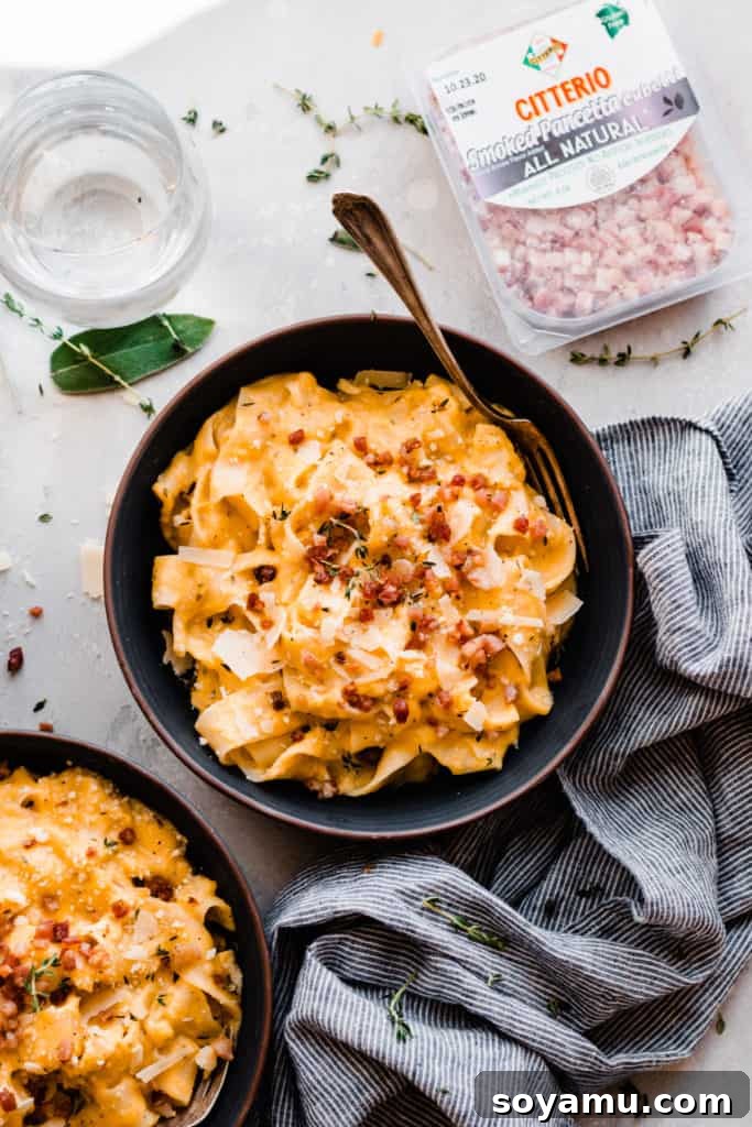 Velvet Butternut Pasta with Savory Pancetta 9 A beautifully presented bowl of creamy butternut squash pasta, generously topped with crispy pancetta, set beside a water glass, scattered fresh herbs, and additional pancetta, inviting diners to indulge.