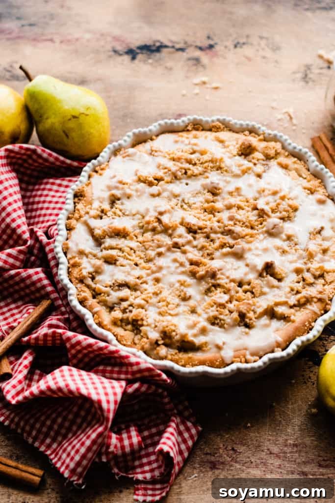 Decadent Deep Dish Pear and Cinnamon Crumble Pizza 2 A deep dish pear dessert pizza drizzled with glaze, on a wooden surface with a red checked linen and fresh pears, ready to be served