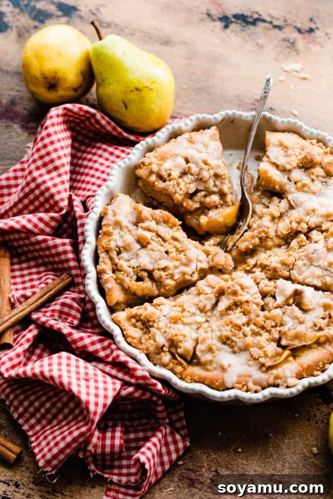 Decadent Deep Dish Pear and Cinnamon Crumble Pizza 11 Sliced deep dish pear dessert pizza in a pie dish on a wooden surface, surrounded by a red checked linen, cinnamon sticks, and fresh pears, showcasing its delicious layers