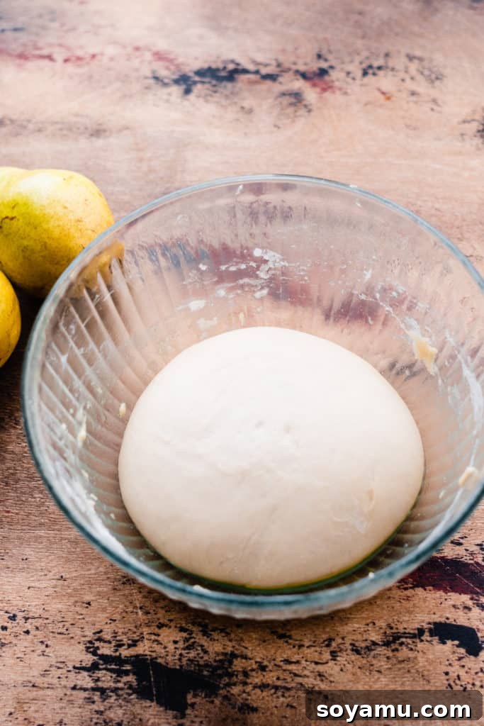 Decadent Deep Dish Pear and Cinnamon Crumble Pizza 4 Risen pizza dough in a glass bowl on a wooden surface, showing its fluffy, expanded state after an hour of rising