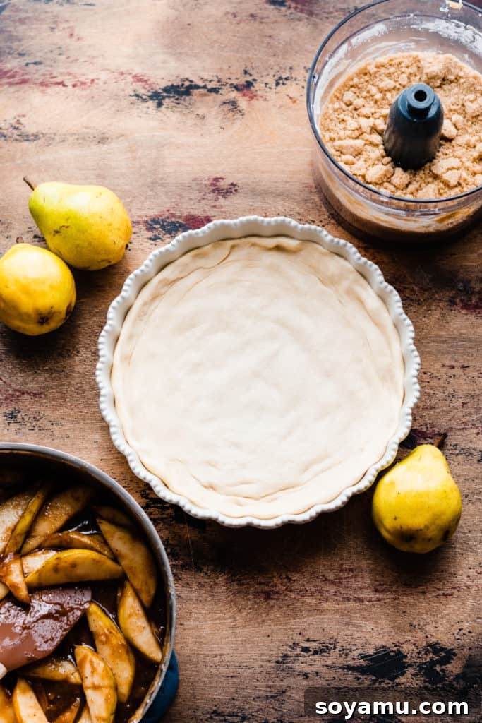 Decadent Deep Dish Pear and Cinnamon Crumble Pizza 7 A pie dish with the pizza crust pressed in, on a wooden surface, surrounded by fresh pears, ready for filling