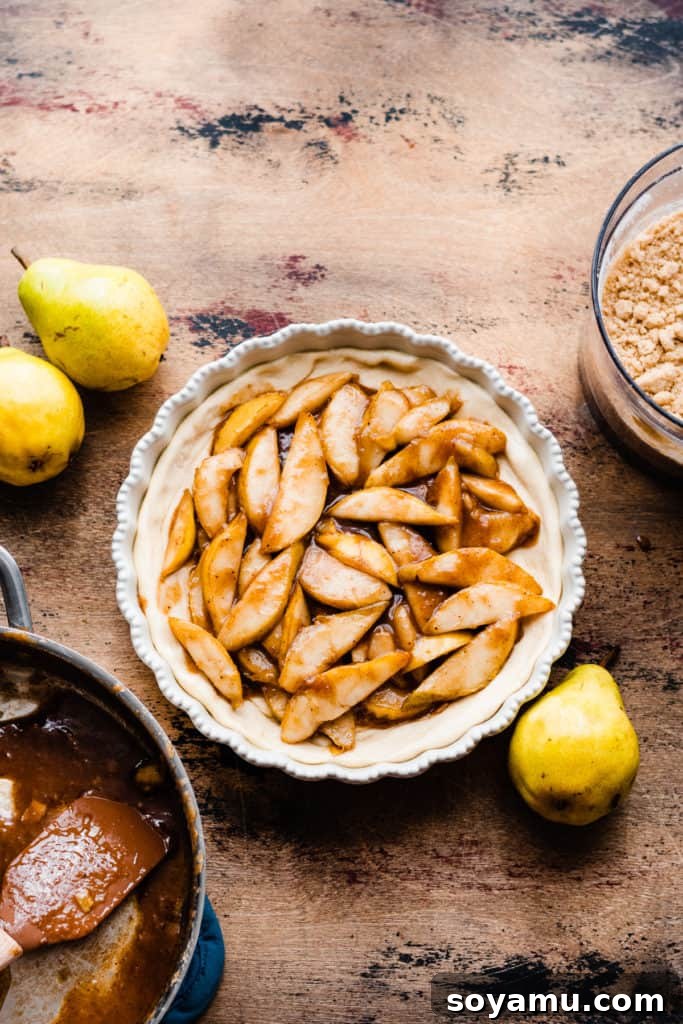 Decadent Deep Dish Pear and Cinnamon Crumble Pizza 8 A pie dish with the pizza crust pressed in and the caramelized pear filling added, on a wooden surface, surrounded by fresh pears