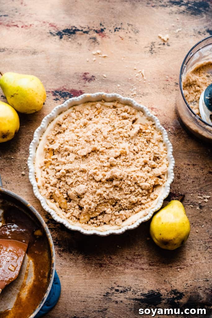 Decadent Deep Dish Pear and Cinnamon Crumble Pizza 9 A pie dish with the assembled, unbaked deep dish pear pizza, topped with a generous layer of cinnamon streusel, on a wooden surface surrounded by fresh pears