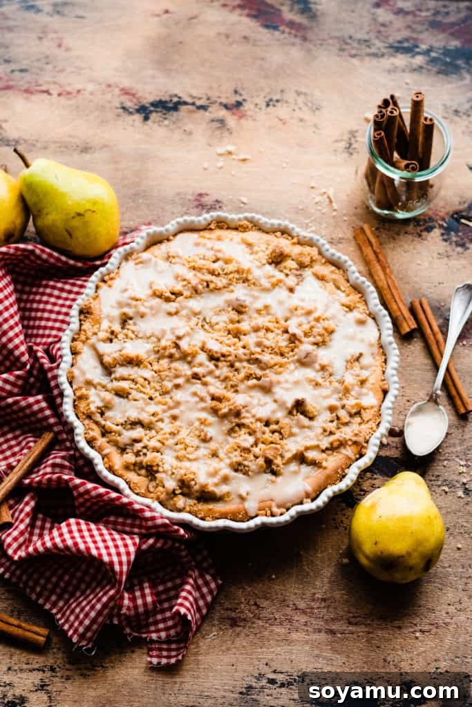 Decadent Deep Dish Pear and Cinnamon Crumble Pizza 10 Pear dessert pizza baked and drizzled with glaze on a wooden surface, surrounded by a red checked linen, cinnamon sticks, and fresh pears, looking utterly delicious