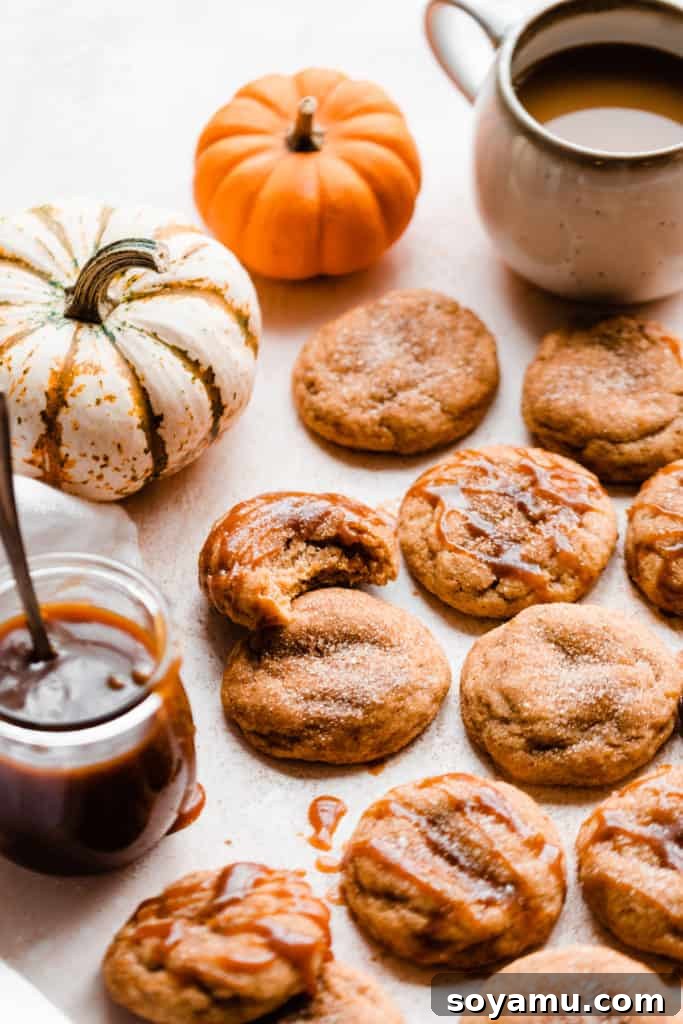 Pumpkin snickerdoodles on a light surface with mini pumpkins, a jar of caramel, and a mug of coffee, showcasing the ultimate fall cookie experience