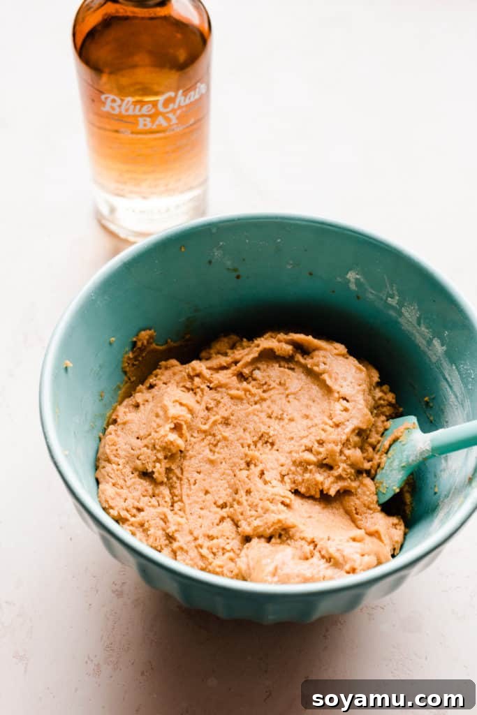 A bowl of pumpkin snickerdoodle cookie dough with a bottle of rum nearby on a light surface, ready for chilling