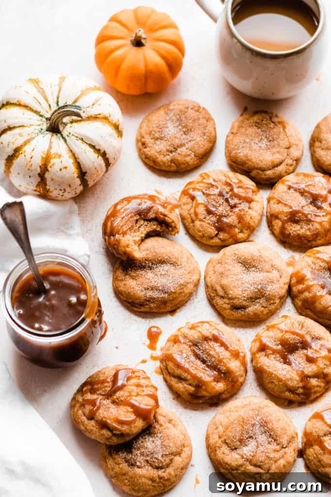 A stunning spread of pumpkin snickerdoodles on a light surface with mini pumpkins, a jar of caramel, and a coffee mug, capturing the cozy autumn vibe