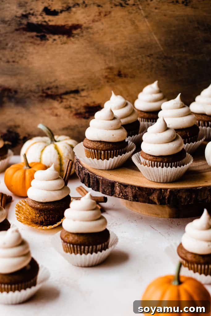 Autumn Pumpkin Delights with Brown Butter Cream Cheese 3 Pumpkin Cupcakes with a swirl of creamy frosting on a wooden cake stand, with mini pumpkins and cinnamon sticks scattered around