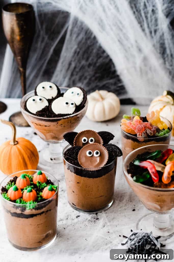 5 dirt cups decorated with oreo ghosts, peanut butter cup bats, a candy pumpkin patch, and gummy worms and spiders