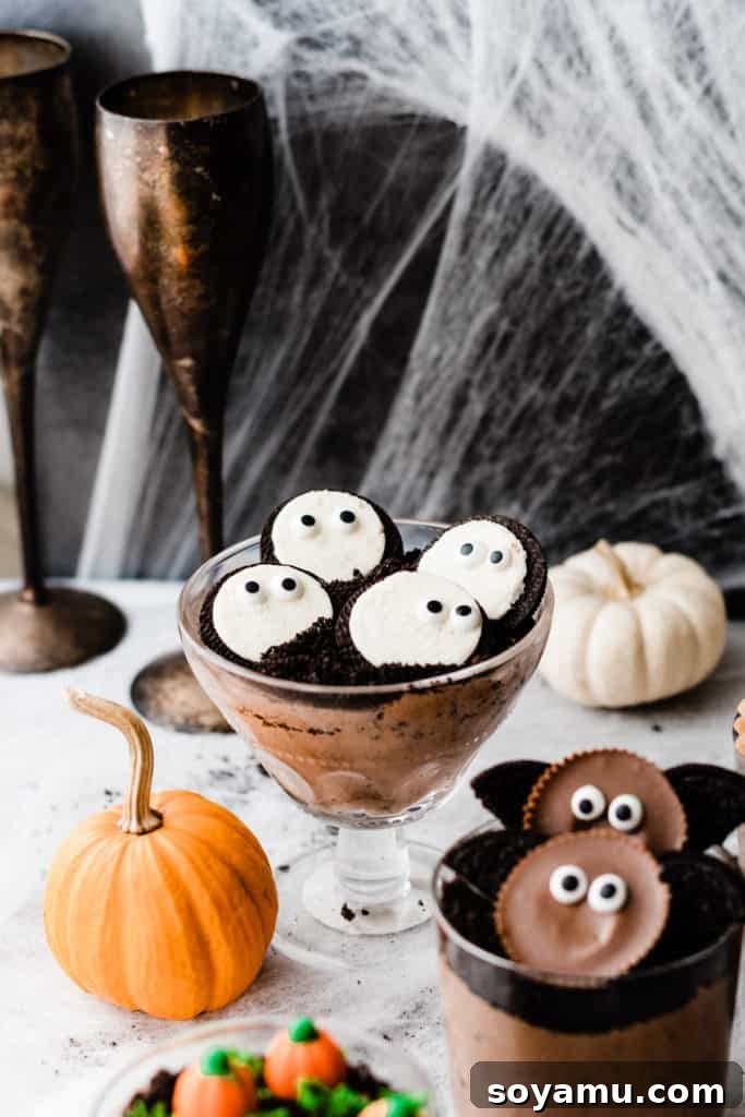 A cup of chocolate filling, oreo dirt, and oreo ghosts, with spider webs and pumpkins in the background