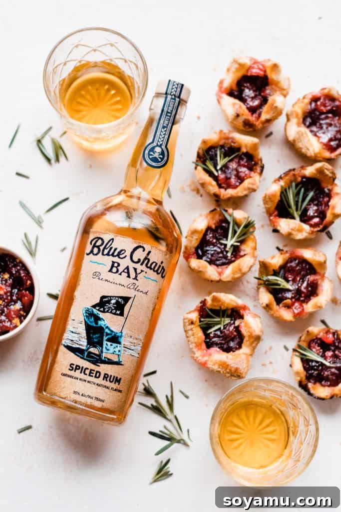Spiced Rum Cranberry and Gouda Puff Pastry Bites 3 A bottle of Blue Chair Bay Spiced Rum on a light surface, flanked by two glasses of rum and the finished puff pastry bites arranged artfully around it.