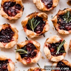 Golden puff pastry bites, freshly baked and garnished with vibrant green fresh rosemary sprigs, arranged elegantly on a light surface, ready to be served.
